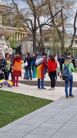 Gyülekező felvonulók a budapesti Erzsébet téren. Egyikőjük köpenyként egy sokszínű Pride zászlót visel.
