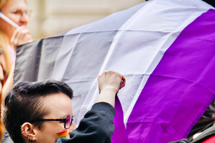 Egy szivárványos arcfestésű felvonuló aszexuális zászlót lenget.