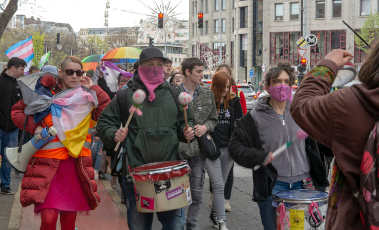 A felvonuló menet eleje egy budapesti úton, többen különböző Pride zászlókat és esernyőket tartanak, ketten dobolnak.